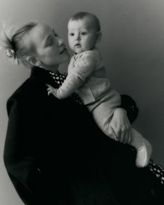 a woman holding a baby in her arms and kissing it's face with both hands