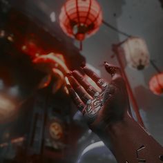 a person holding their hand out in front of red lights and lanterns hanging from the ceiling