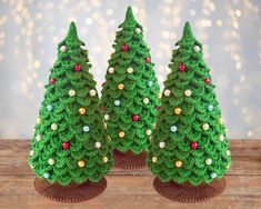 three small crocheted christmas trees sitting on top of a wooden table next to each other