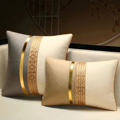 two decorative pillows on a white couch in front of a mirror with gold trimmings