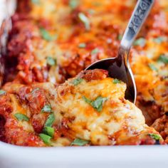 a spatula scooping some food out of a casserole dish with meat and cheese