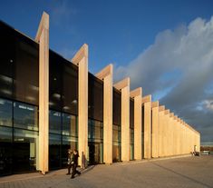 two people walking past a large building with tall columns on the outside and glass windows