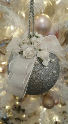 a silver ornament with white flowers and pearls hanging on a christmas tree in front of ornaments