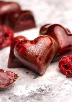 two pieces of heart shaped candy next to some raspberries on a white surface