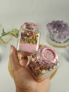 two small glass jars filled with different types of flowers and herbs on top of each other