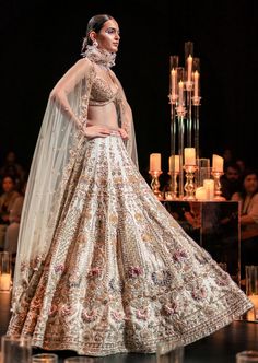 This enchanting earthy beige lehenga set is a beautiful blend of exuberance and grandeur. An ensemble that you will want this wedding season includes a lehenga, a blouse, a dupatta and a veil. Stitched to perfection, the lehenga features 3D embroideries with organza flowers using pearls, salli, cutdana, and stud tassels. The sleeveless blouse features a scintillating sweetheart neckline with handcrafted finish and a back hook closure. Paired with a heavy net dupatta, the cut-work detailing and intricate embroidery take center-stage. The lehenga comes with an attached cancan and the blouse has padding. Completed with a veil, this opulent ensemble silhouette will glimmer in the spotlight. Dry-clean only if required. Slight variation in color is possible due to digital photography. Cream Hand Embellished Lehenga For Reception, Hand Embellished Cream Lehenga For Reception, Floor-length Lehenga With Intricate Embroidery For Wedding Reception, Anarkali Floor-length Gown For Wedding Reception, Intricate Embroidery Floor-length Gown For Wedding Reception, Floor-length Gown With Intricate Embroidery For Wedding Reception, Floor-length Embroidered Gown For Wedding Reception, Elegant Lehenga With Intricate Embroidery For Wedding Reception, Elegant Lehenga With Dupatta For Wedding Reception