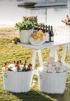 two white buckets filled with wine bottles next to an outdoor table full of food and drinks