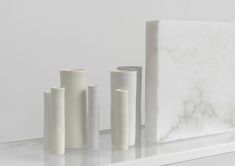 several white vases sitting on top of a shelf next to a marble block wall