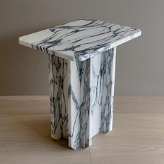 a white and black marble side table sitting on top of a wooden floor next to a wall