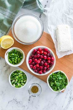 ingredients for cranberry sauce laid out in bowls on a cutting board, including lemons, parsley and sugar