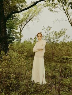 a woman is standing in the woods with her arms crossed