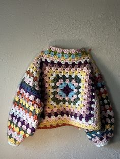 a colorful crocheted sweater hanging on the wall next to a white brick wall