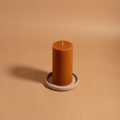 an orange candle sitting on top of a white plate next to a brown tablecloth