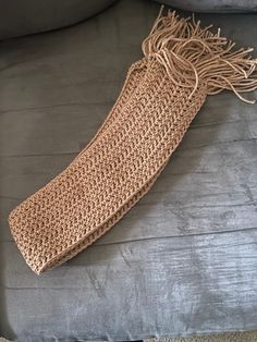 a crocheted scarf laying on top of a gray couch next to a pillow