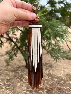 a hand holding a brown and white feather keychain in front of a tree