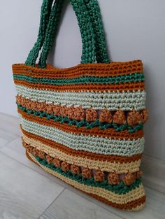 a multicolored crocheted bag hanging on a wall next to a wooden floor