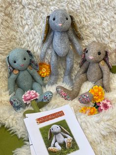 three stuffed animals sitting next to each other on a white rug with flowers and an open book