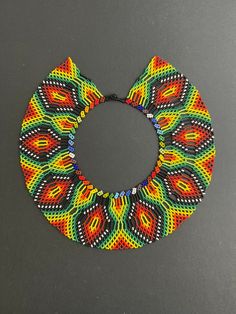 "This Trendy Multicolor Oversized Necklace was made using ancestral beading techniques by the Embera Chami tribe of Colombia. Their pieces are all handmade, and the designs and colors used are unique to their tribe and related to their everyday lives.   This stunning one-of-a-kind Retro Necklace would surely make your outfit pop and is the perfect eye-catching piece needed to complete your look.  Colors: Greens, Black, Reds, Yellows, Orange, and Blues  Length:16\" Width: 3\" Check out other simi Traditional Colorful Beads Bib Necklace, Multicolor Fair Trade Beads For Festival, Traditional Colorful Beads For Crafting, Traditional Handmade Bib Necklace With Round Beads, Traditional Handmade Multicolor Beads, Multicolor Festival Beads, Traditional Handmade Multicolor Beaded Necklaces, Bohemian Rainbow Beads For Jewelry Making, Rainbow Bohemian Beads For Jewelry Making