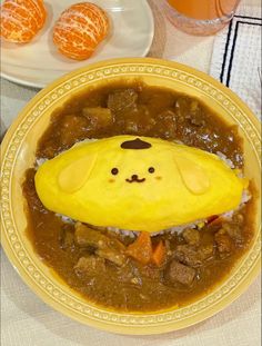 a yellow plate topped with meat and vegetables covered in a cartoon face on top of it