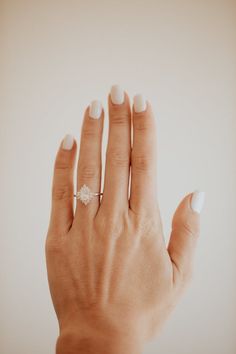 a woman's hand with a diamond ring on her left hand and white nail polish