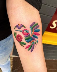 a colorful tattoo on the arm of a woman's left leg, with flowers in the shape of a heart