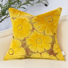 a yellow floral pillow sitting on top of a white couch next to a potted plant