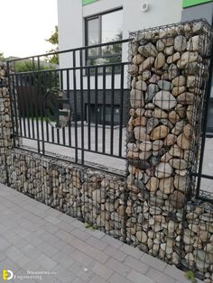 there is a fence made out of rocks on the side of the street with a black gate