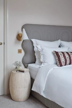 a bed with white sheets and pillows in a bedroom next to a door that has a striped headboard on it