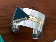 "Stunning cuff bracelet designed by M & J Savitt. Sterling & 14 karat gold with a triangle shaped black onyx set in a 14 karat bezel & gold inlaid stripe. Signed and stamped. Measures approximately 1 1/8\" wide." Modern Black Enamel Jewelry, Unique Polished Cuff Jewelry, Modernist Cuff Jewelry For Gift, Black Polished Cuff Bracelet For Formal Occasions, Formal Black Cuff Bracelet With Polished Finish, Modern Black Bangle Jewelry, Formal Black Polished Cuff Bracelet, Modernist Cuff Jewelry With Polished Finish, Gold Sterling Silver Cuff Jewelry