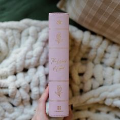 a person holding up a pink tube with gold writing on it and a white blanket in the background