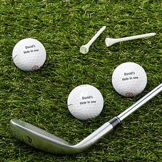 three golf balls and a club on the grass with some words written on them,