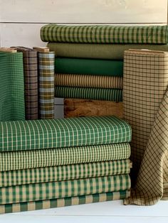 a stack of green and brown plaid fabric sitting on top of each other in front of a white wall