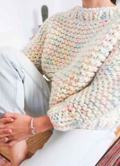 a woman sitting on top of a bed wearing a sweater