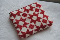 a small red and white purse sitting on top of a bed next to a pillow