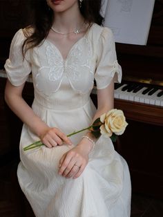 a woman in a white dress is holding a flower and sitting next to a piano