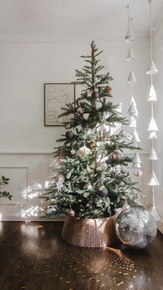 a small christmas tree in a room with wooden flooring and white ornaments hanging from the ceiling