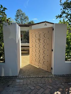 an open wooden door on the side of a white building with trees in the background