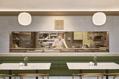 an empty restaurant with tables and chairs in front of the counter, behind which a cook is preparing food