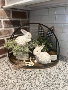 two white rabbits sitting on top of a shelf next to some plants and eggs in a vase