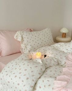 a bed with pink comforters and pillows on top of it next to a night stand