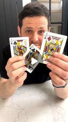 a man sitting at a table holding up four playing cards in front of his face