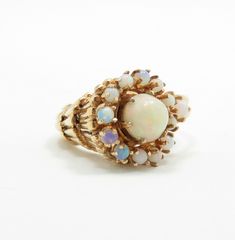 14k yellow gold 7mm round natural opal cabochon 12 2mm round natural opals size 7.25 (sizable) condition: excellent Fabulous opal statement ring from the midcentury, crafted of 14 karat yellow gold.  The ring is in the shape of a cornucopia, with beautiful natural opals just spilling out!  At the center of the setting is a 7mm round, domed opal with beautiful pink opalescence.  A halo of twelve 2mm opals surround the center stone, with an additional 3mm opal thrown in for good measure.  This rin Vintage Opal Round Rings, Antique Style Round Opal Ring, Heirloom 14k Gold Opal Ring, Heirloom Style Round Opal Ring, Heirloom Style Opal Ring, Heirloom Opal Ring, Antique Yellow Gold Round Opal Ring, Fine Jewelry Opal Ring With 17 Jewels, Heirloom Yellow Gold Round Opal Ring