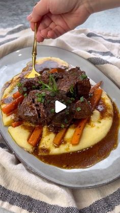 a person is holding a fork over a plate of food with gravy and carrots