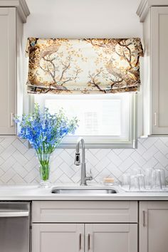 a kitchen with white cabinets and blue flowers on the window sill above the sink