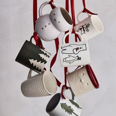 coffee mugs hanging from a red ribbon on a white wall with trees and animals