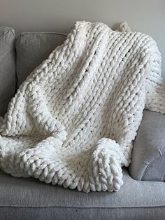 a white knitted blanket sitting on top of a gray couch next to a pillow