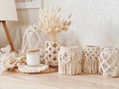 three white crocheted vases sitting on top of a wooden table next to a candle