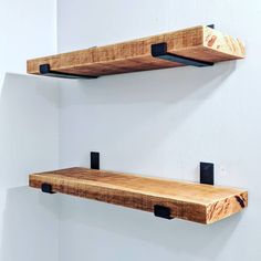 two wooden shelves with black metal brackets on the wall next to each other in a white room