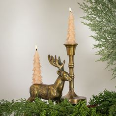 a brass deer figurine next to a candle holder with pine cones on it