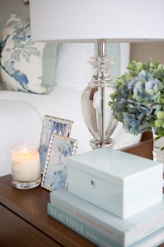 a table with a lamp, flowers and pictures on it next to a box that has a candle in it